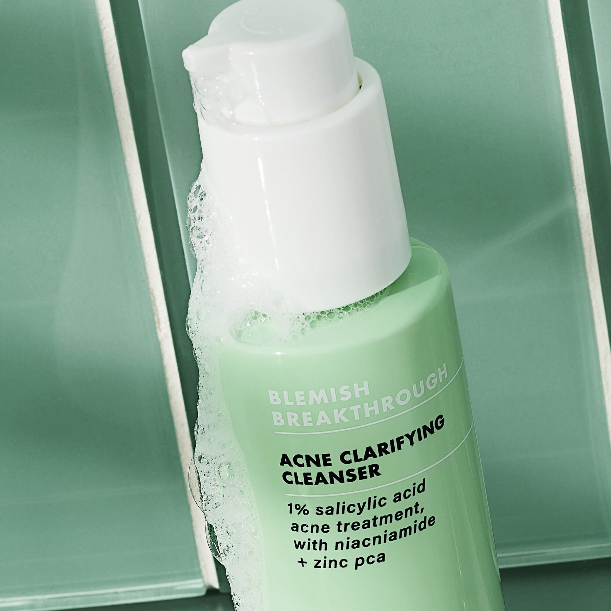 Green bottle of Acne Clarifying Cleanser with white pump on a green background